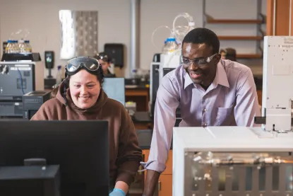 Male faculty member looking at a computer in a lab with a female student