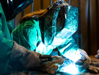 Two people in welding masks working with welder on a table