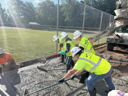 Four students in fluorescent shirts and vest and hardhats laying cement