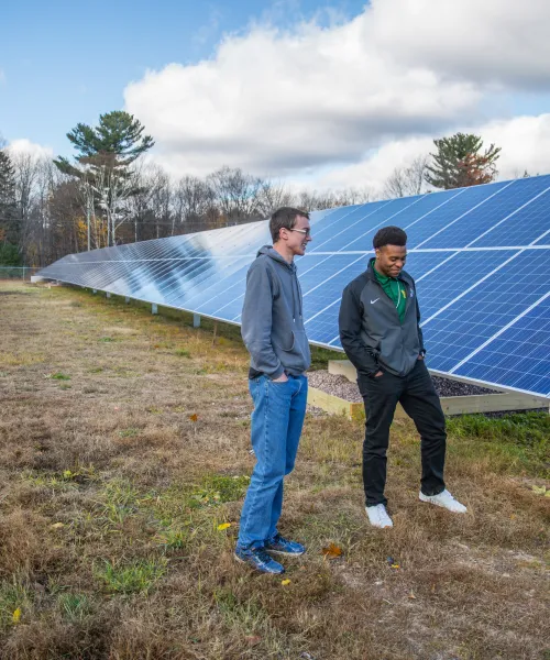 two male students talking to a male instructor while standing in front of solar panels 