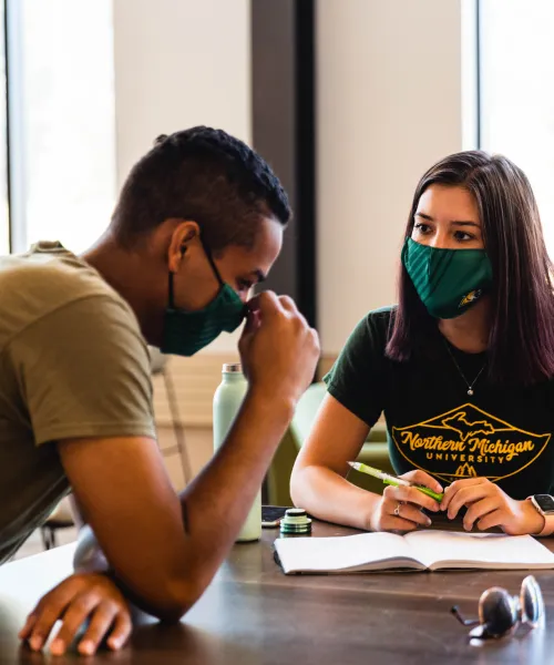 Two students with masks on studying inside