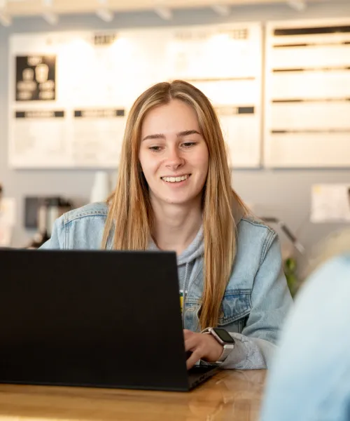 Student with long blonde hair sitting at table with laptop in front of her