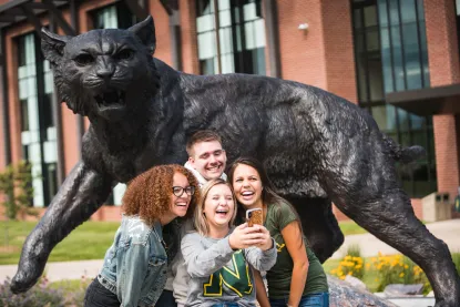 Four students taking a selfie in front of NMU's Wildcat Statue
