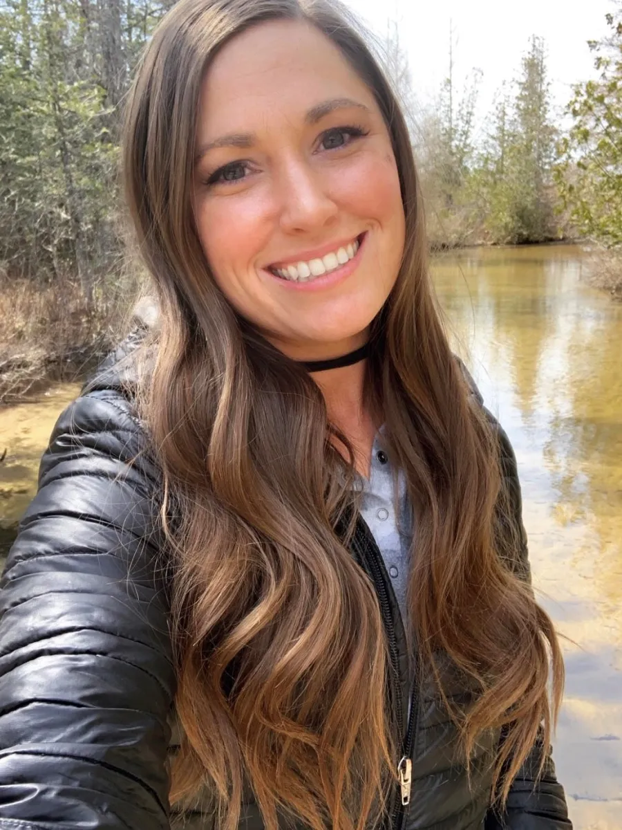 Smiling woman with long brown hair, water and trees in the background