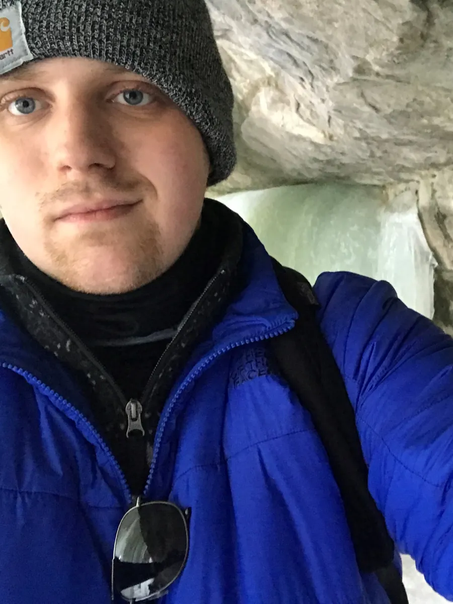 Man in a gray cap and blue jacket, standing in an ice cave