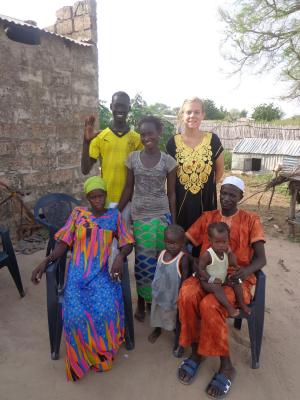 Kaitlin McDonald, a woman in a black and gold dress, stands with two people behind two seated adults. Two children sit on the lap of one of the seated adults. The group is positioned in front of a brick wall.