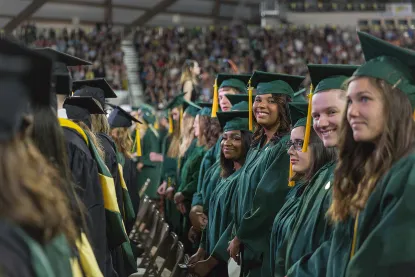 Crowd of students at graduation with some facing the camera and smiling