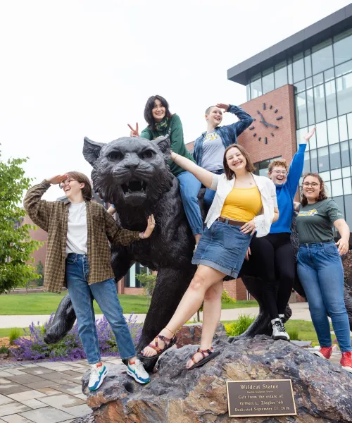 five students standing with the Wildcat statue on NMU's campus