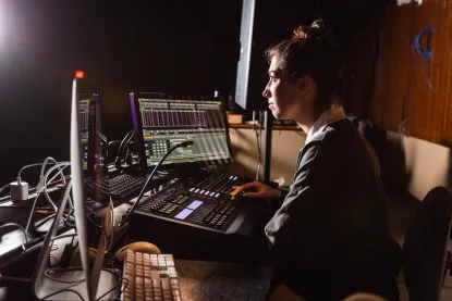 A student sits at a lighting console